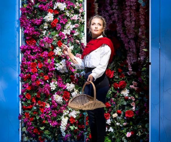Soprano, Alexandra Oomens, performing onstage infront of a floral backdrop, holding a picnic basket at City Recital Hall