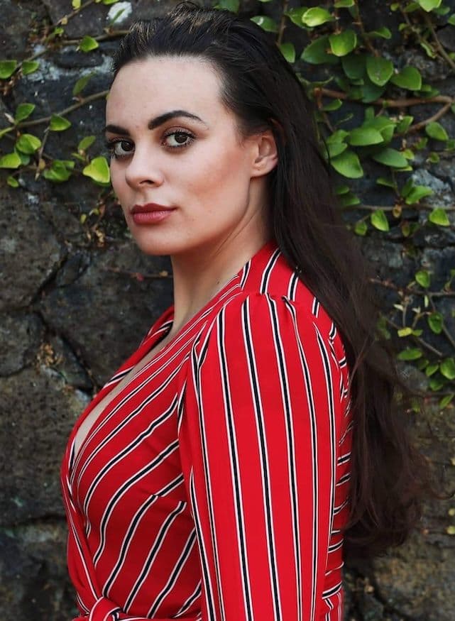 Headshot portrait of Madison Nonoa Soprano dressed in a red pinstripe jacket. She has long dark hair