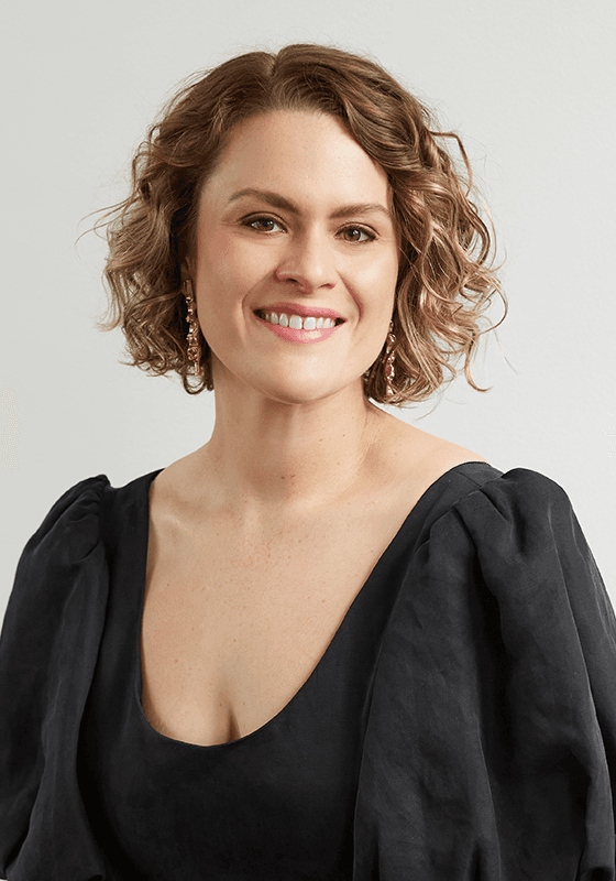 Stephanie Dillon, mezzo-soprano from Moree, now in Sydney, known for her versatile voice, acclaimed in Baroque to contemporary music. She is smiling with short curly hair and earrings